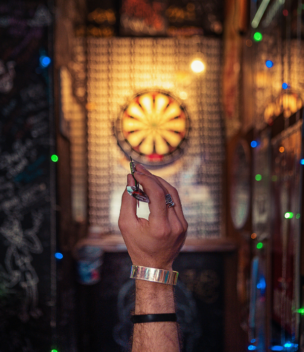 A man's hand preparing to launch a dart toward a target