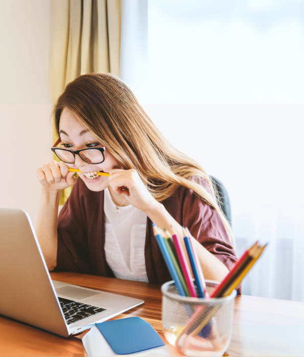 Girl biting a pencil while staring at her computer screen.