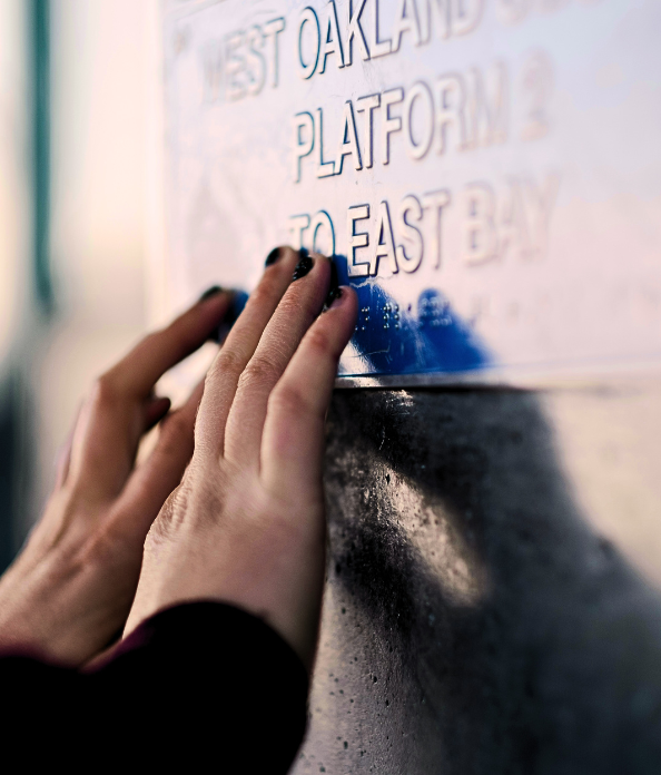 Two hands reading a Braille train station sign