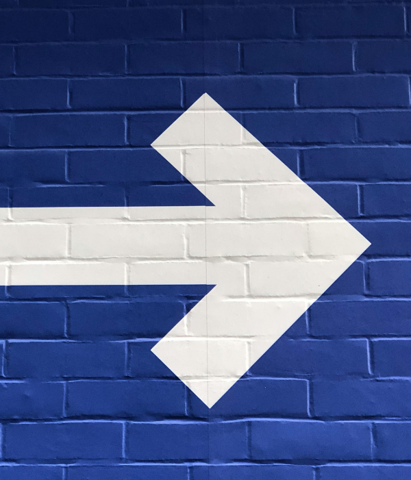 Brick wall painted blue with a painted white arrow pointing to the right